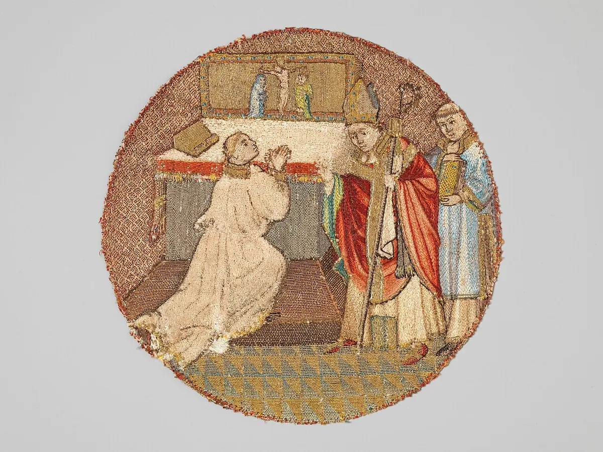 Circular Flemish embroidery of a young man kneeling in a white robe before an altar while a bishop in a red cope stands over him, with a cleric behind