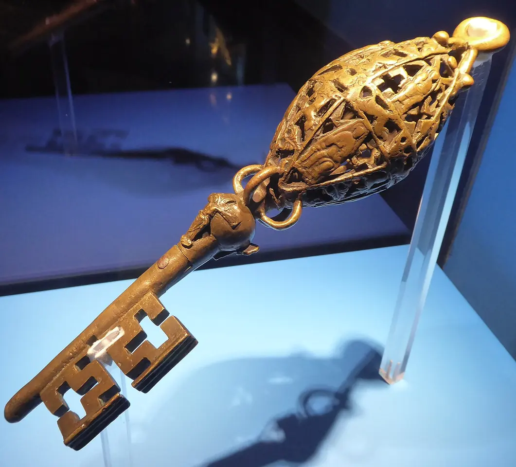 A large bronze key with an openwork oval handle displayed on a clear stand against a blue background