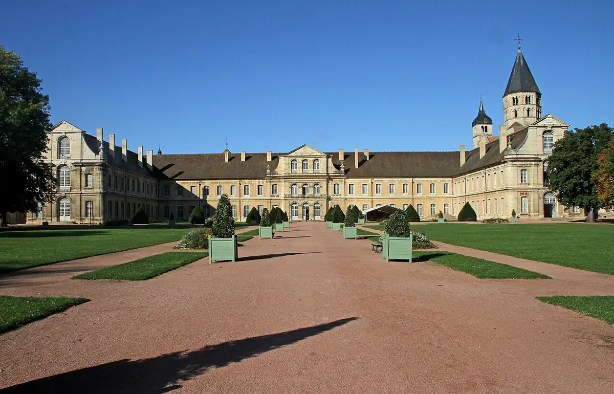 A long eighteenth-century abbey building facing a garden walk, with a tall octagonal Romanesque bell tower rising behind it