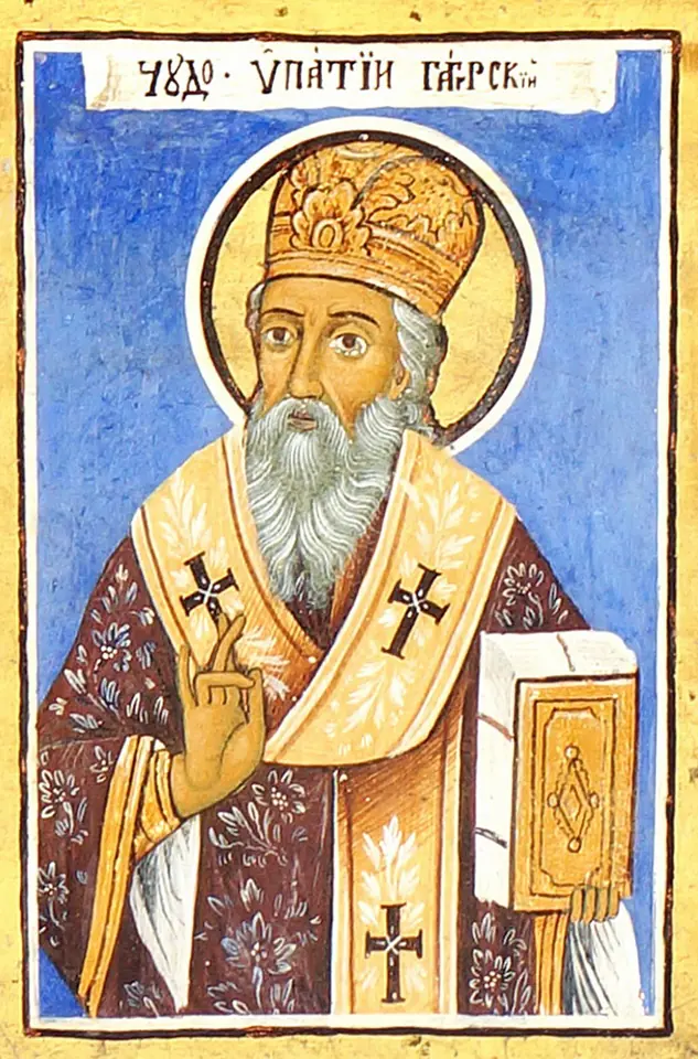 A brightly painted icon of a white-bearded bishop in a jeweled miter and crossed vestments, blessing with one hand and holding a gold Gospel book