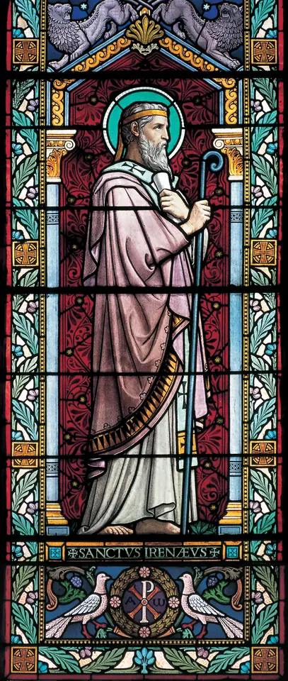 Stained-glass window of a white-bearded bishop with a halo and crozier, in a pale tunic and red cope, labeled Sanctus Irenaeus