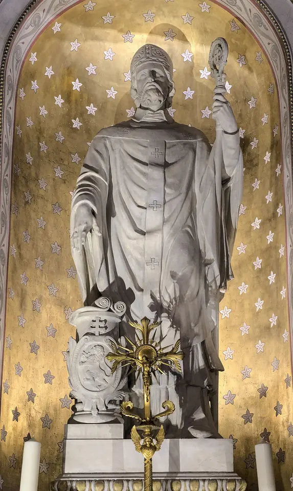 White marble statue of a bishop in miter and cope holding a crozier, standing in a gold-starred niche above an altar
