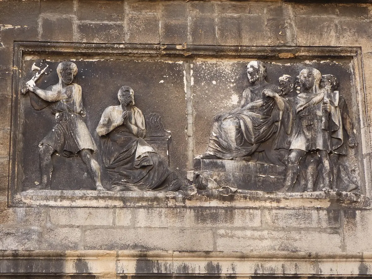 Weathered stone relief of a kneeling bishop before a soldier raising a sword, with a Roman magistrate seated among soldiers at the right