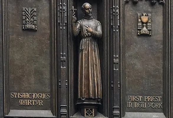 Bronze relief of a Jesuit holding a crucifix in a narrow panel, with the words St. Isaac Jogues Martyr and First Priest in New York