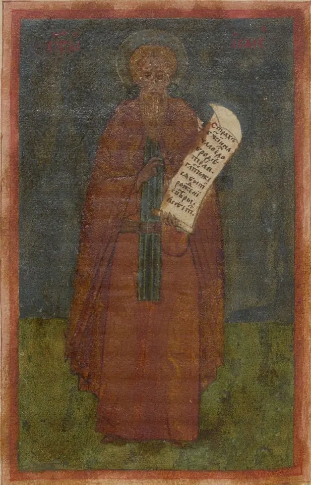 A brightly colored Russian manuscript miniature of a monk in a blue hood and golden-brown robe writing in a book at a carved desk, framed by red buildings and a blue floral border
