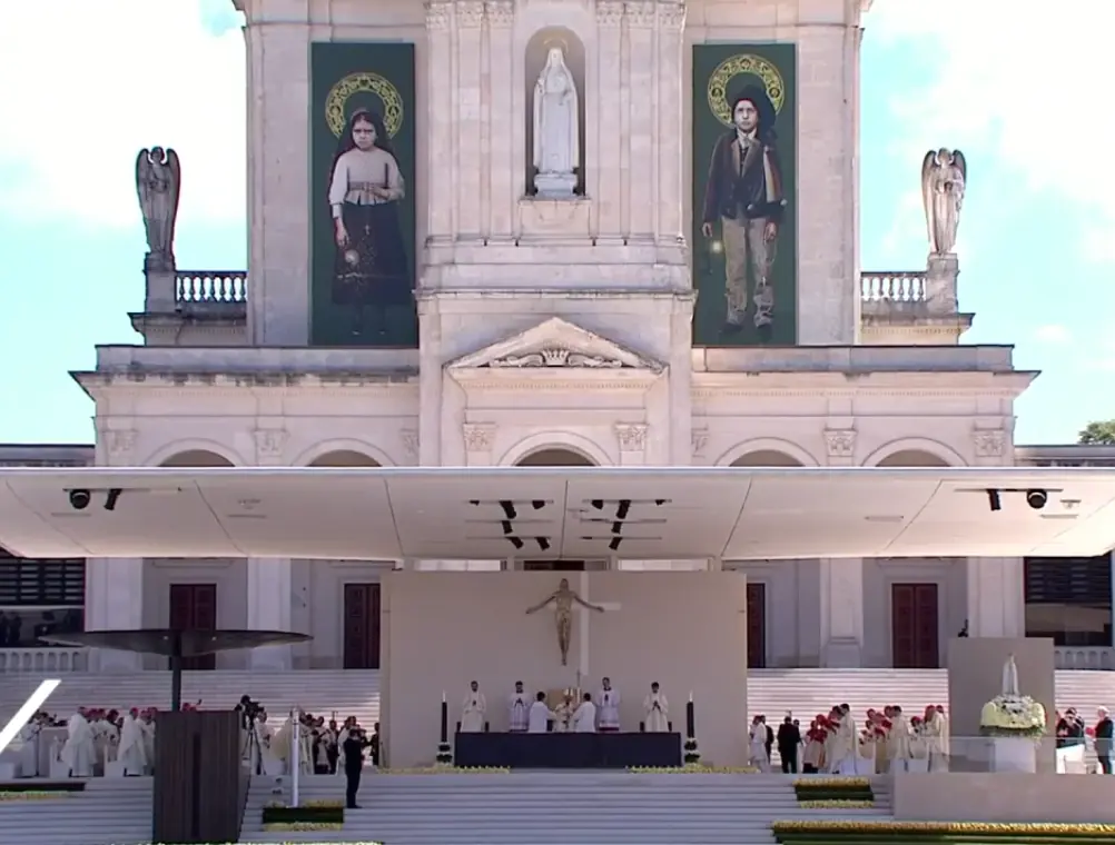 The white facade of the Basilica of Our Lady of the Rosary hung with two large portraits of the shepherd children, above an outdoor altar where the canonization Mass is being celebrated