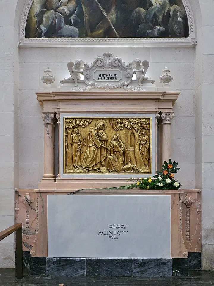 A white marble tomb in a side chapel, carved with the name Jacinta, beneath a gilded relief and an arched painting, with flowers on top