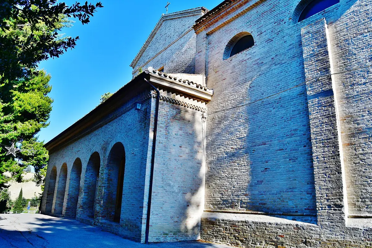 The side of a long brick church with a row of round arches along a portico, under a deep blue sky