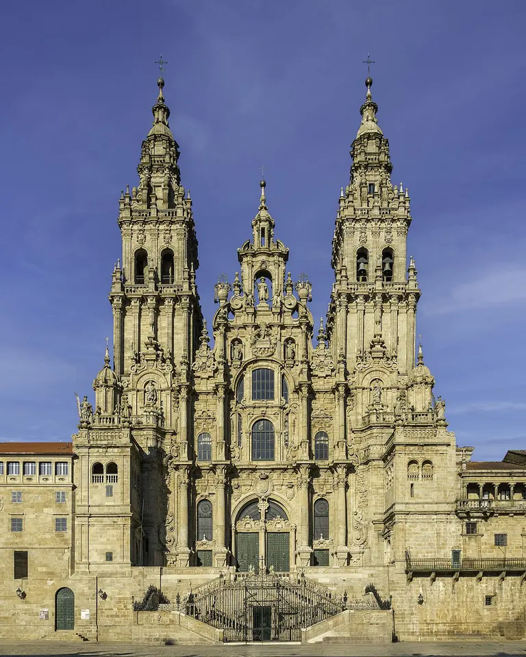 The tall Baroque granite west front of Santiago Cathedral with two ornate bell towers and a double staircase, under a blue sky