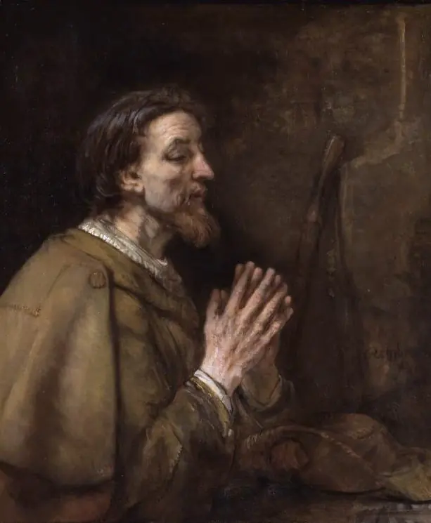 Rembrandt painting of an aging, bearded St. James in a brown cloak with a white collar, praying with folded hands, with a pilgrim's hat and staff behind him