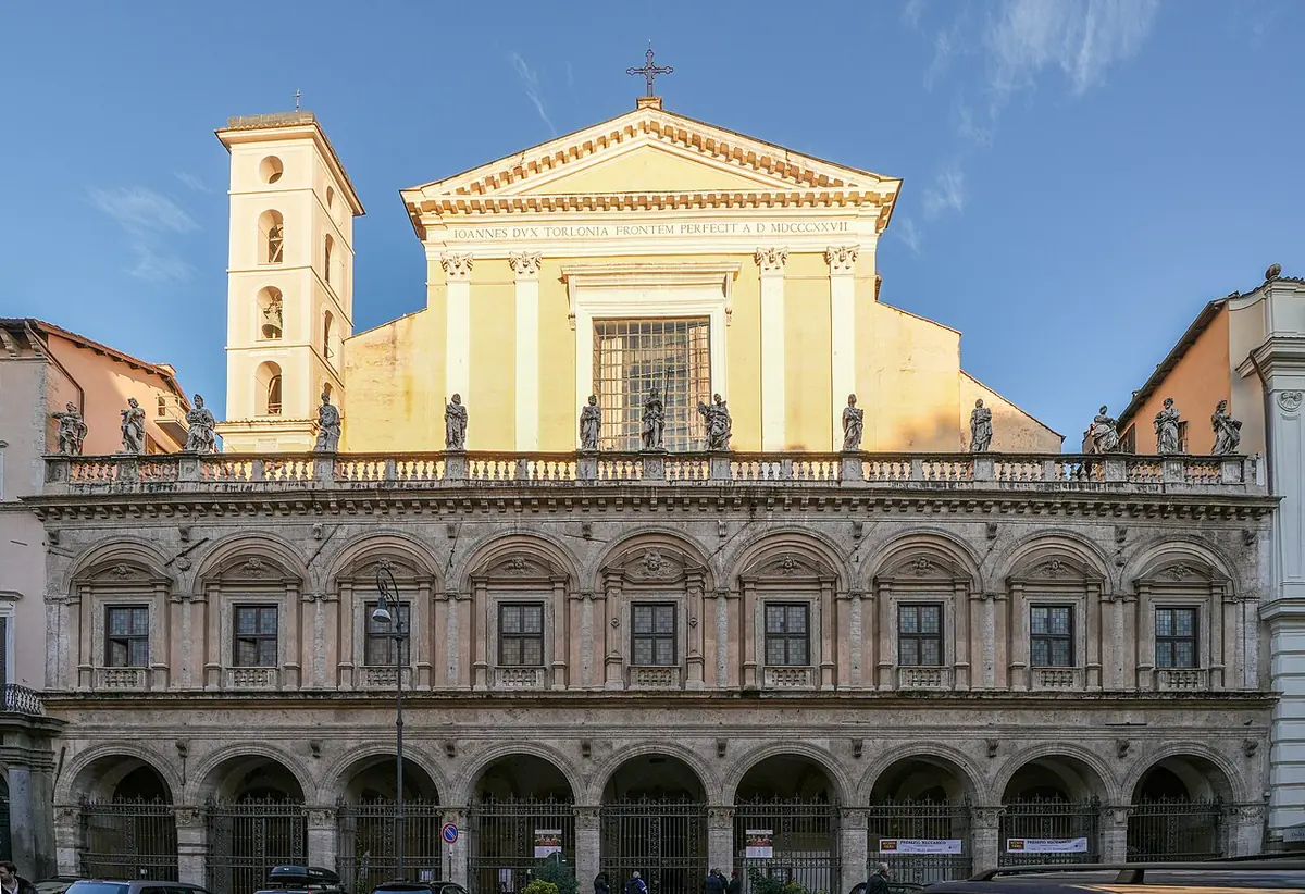 The arcaded Renaissance portico and pale neoclassical upper facade of the Basilica of the Holy Twelve Apostles in Rome under a blue sky