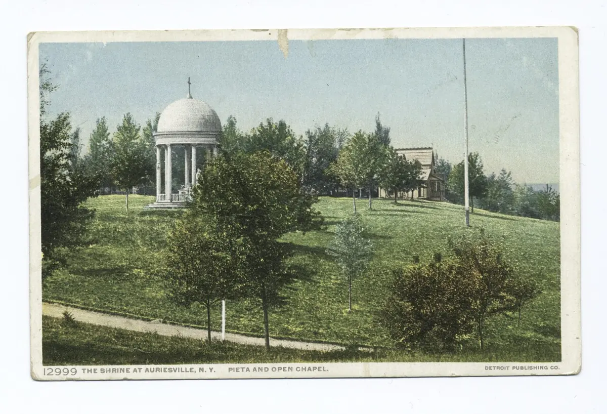Colored early 20th-century postcard of a small domed open chapel with white columns on a grassy hillside among trees at the Auriesville shrine