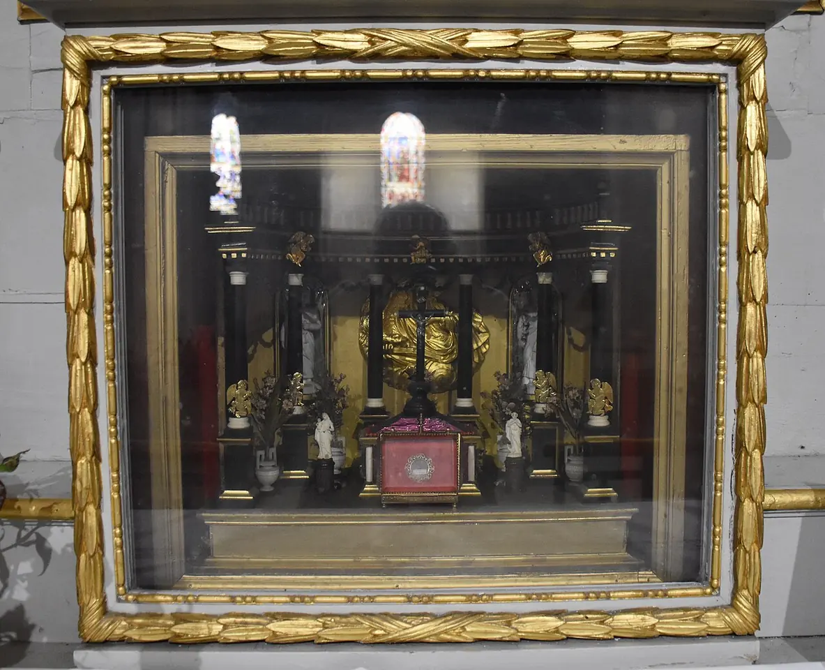 A gilded glass-fronted case in a church holding a small model of a golden altar with a red relic cushion at its center