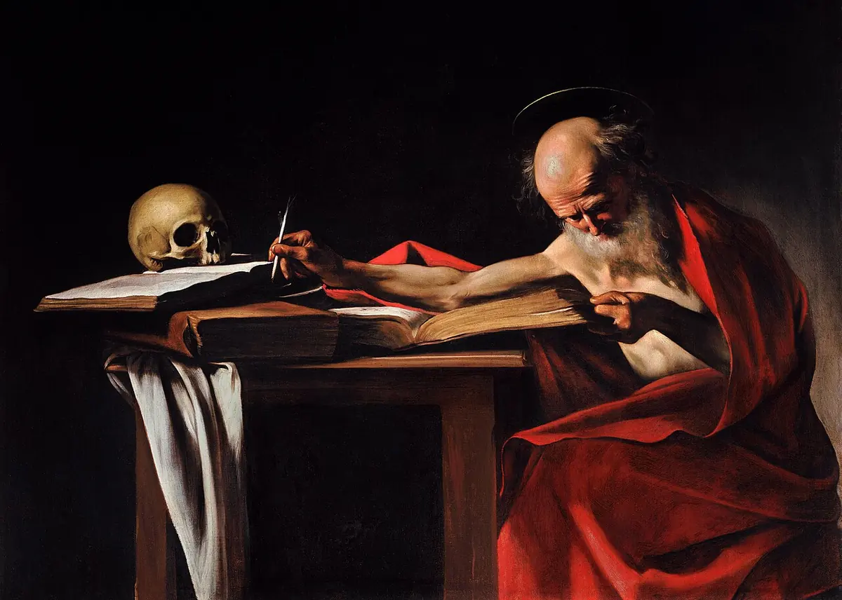Painting of a bald, white-bearded old man in a red cloak stretching his arm across a table to dip his pen, reading a large book, with a skull on the books opposite him