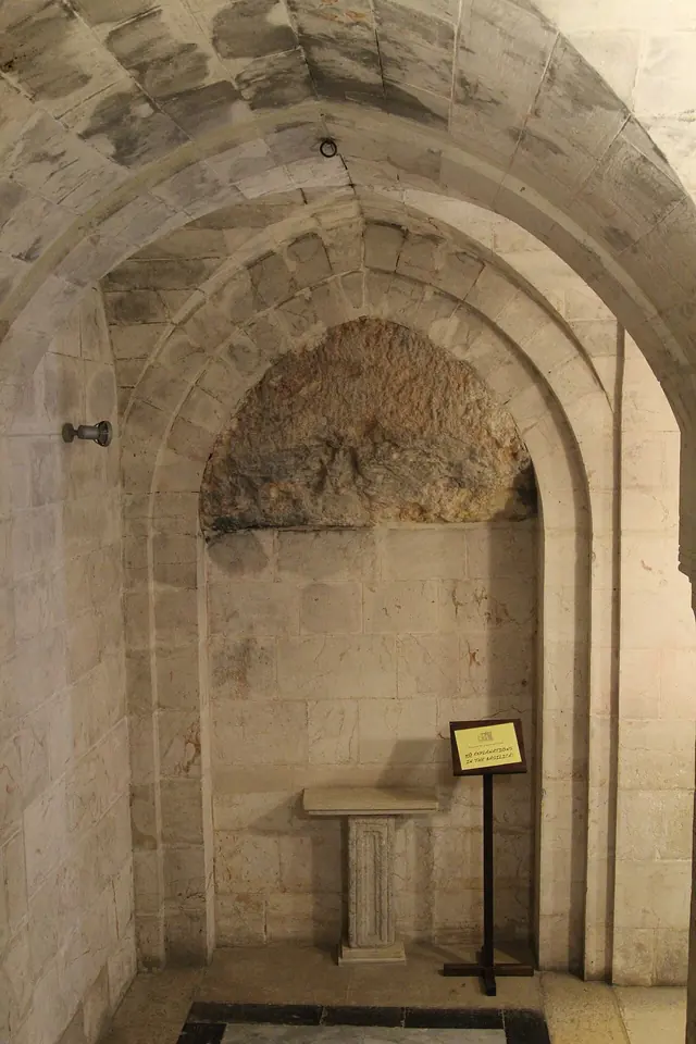 A small arched stone crypt with a rough rock wall at the back and a plain lectern