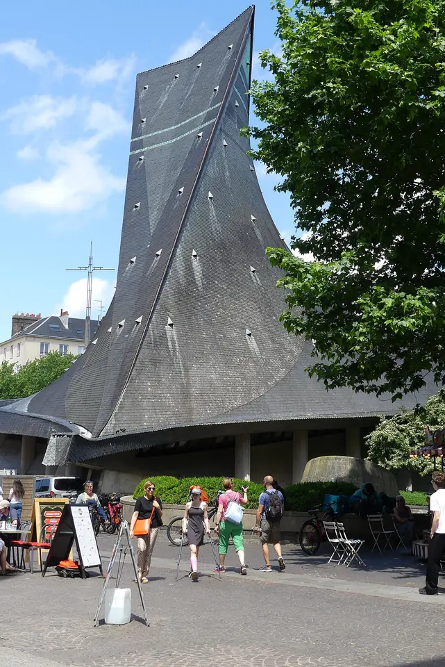 Modern church with a sweeping dark slate roof that rises to a sharp point like a flame, above a busy pedestrian square