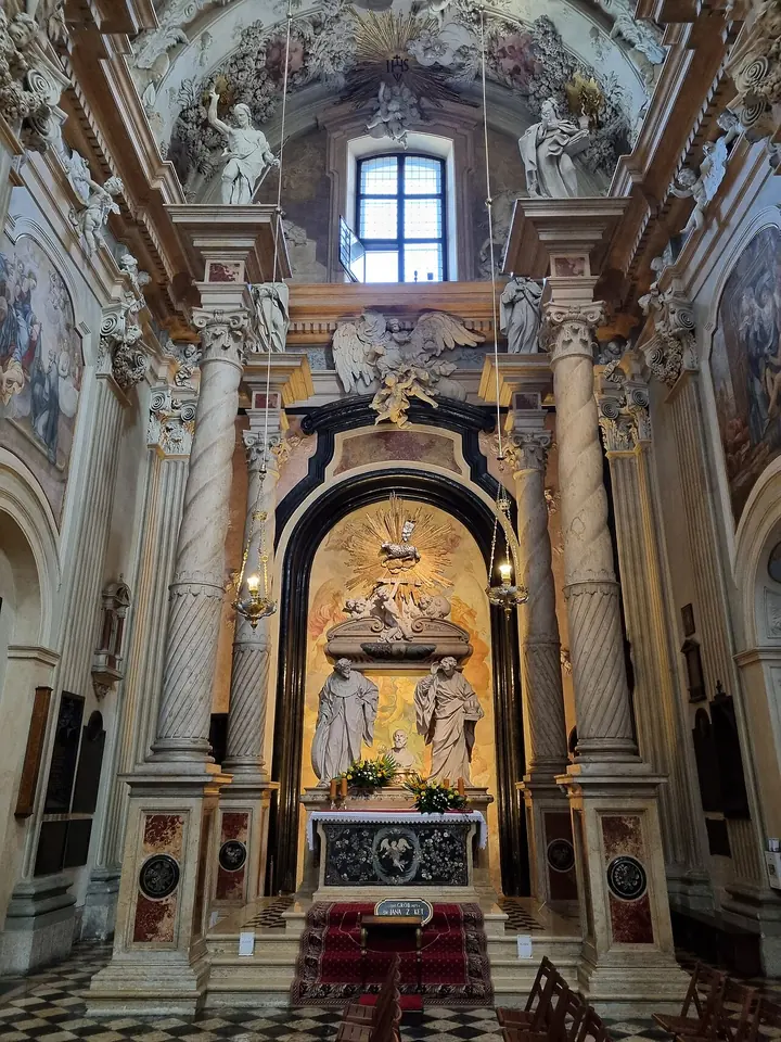 Baroque marble tomb of St. John Cantius under a tall arch with twisted columns, the sarcophagus carried on the shoulders of four figures