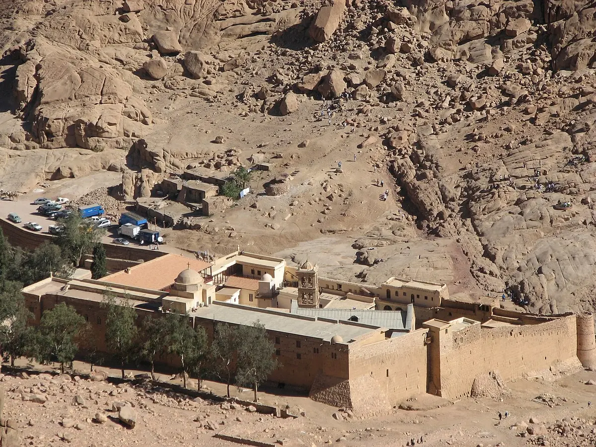 The fortified stone walls and buildings of St. Catherine's Monastery seen from above, in a dry valley among rocky mountain slopes