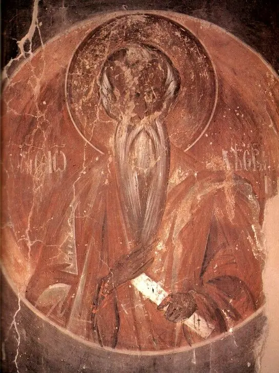 A worn fresco medallion in reddish-brown tones of a monk with a long beard and a stern face, holding a small white scroll