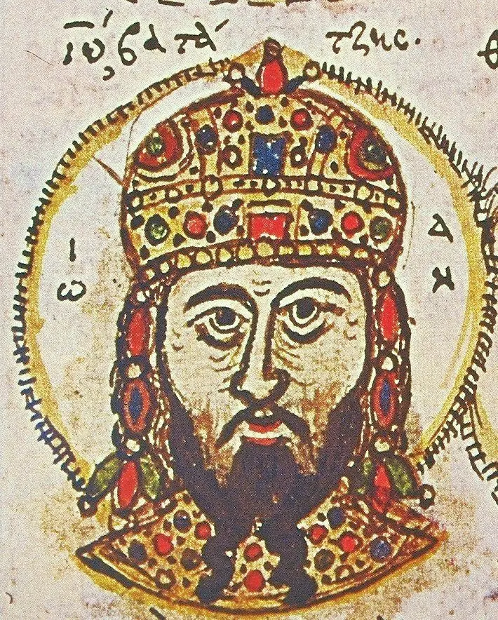 Medieval manuscript miniature of a bearded emperor's head and shoulders in a tall jeweled crown with hanging pendants, inside a gold halo-like circle with Greek letters
