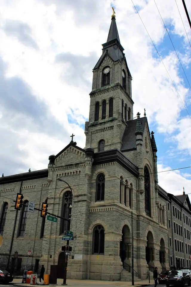 Tall gray stone Victorian church with a pointed bell tower on a Philadelphia street corner under a cloudy blue sky