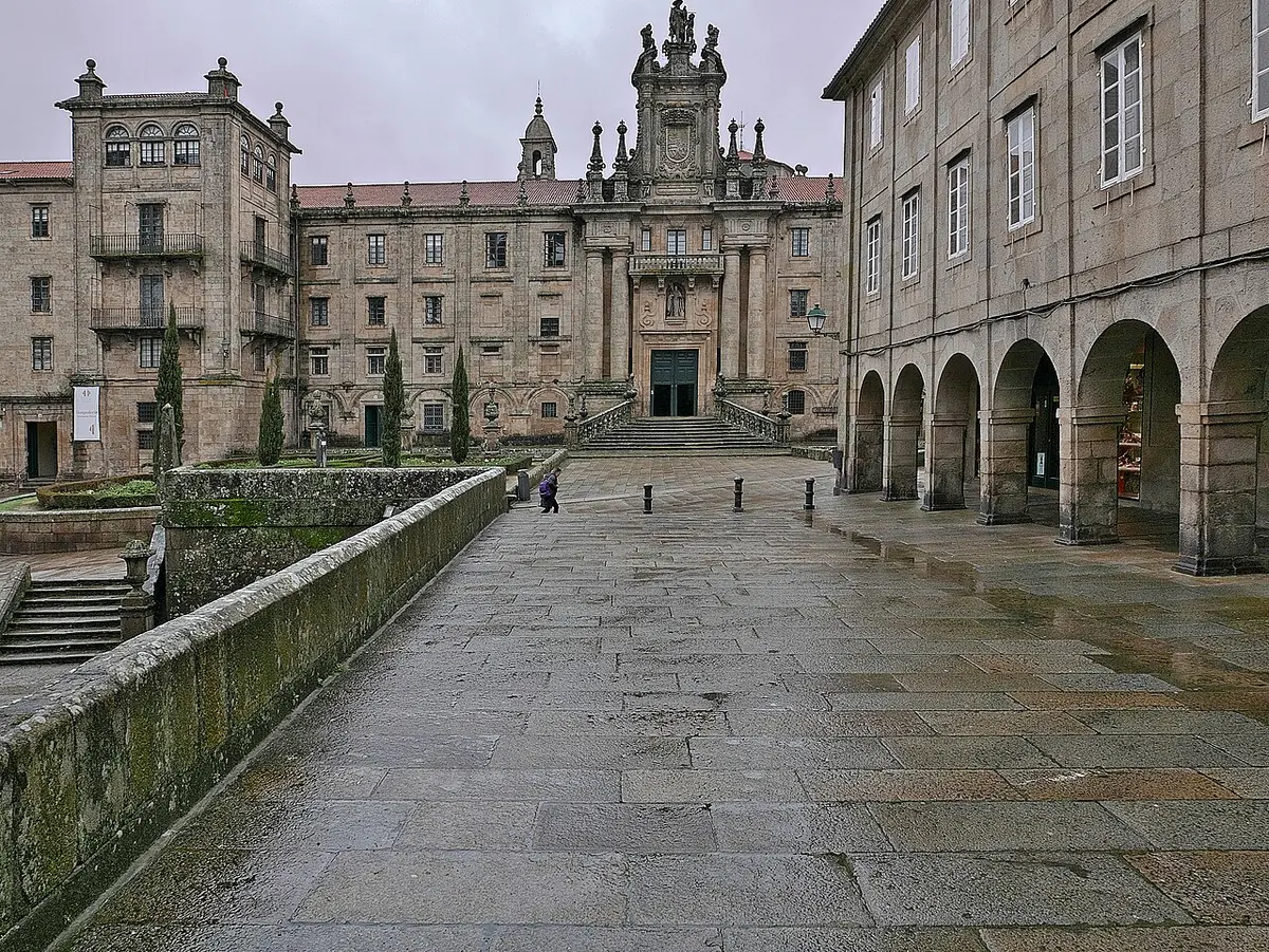 The long gray granite facade of a great Baroque monastery at the end of a wide wet stone courtyard