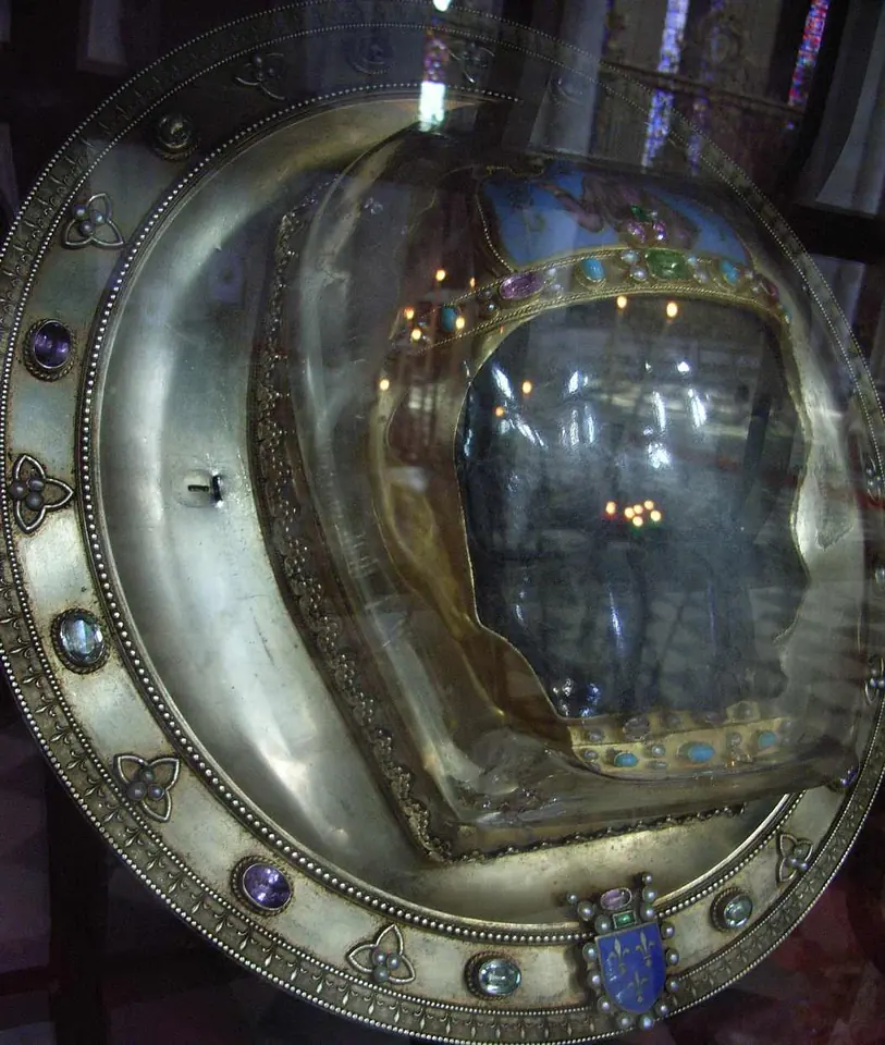 Plato redondo de plata dorada adornado con joyas que contiene la parte frontal de un cráneo bajo una cubierta de cristal de roca con una pequeña corona de oro