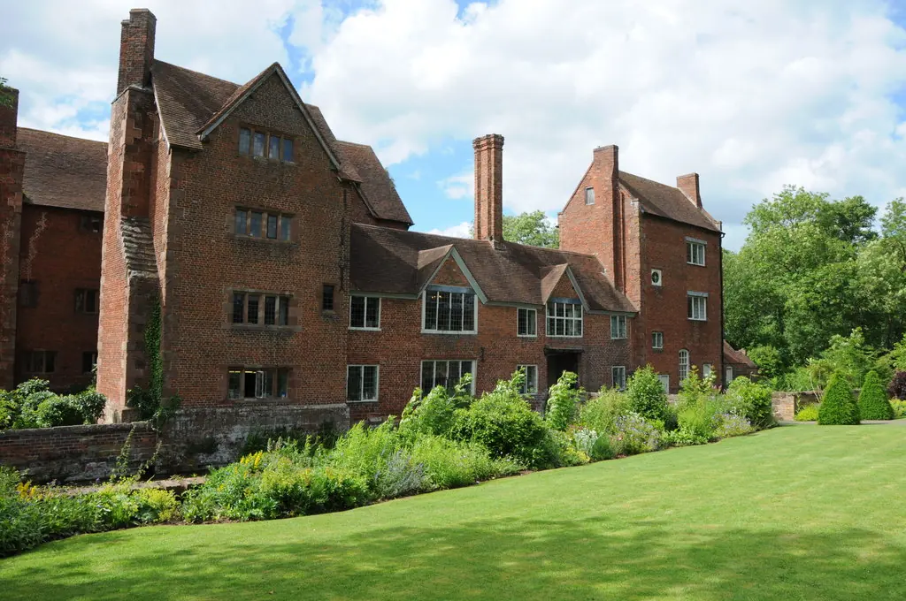 A tall red-brick Elizabethan manor house with tall chimneys behind a lawn and flower borders