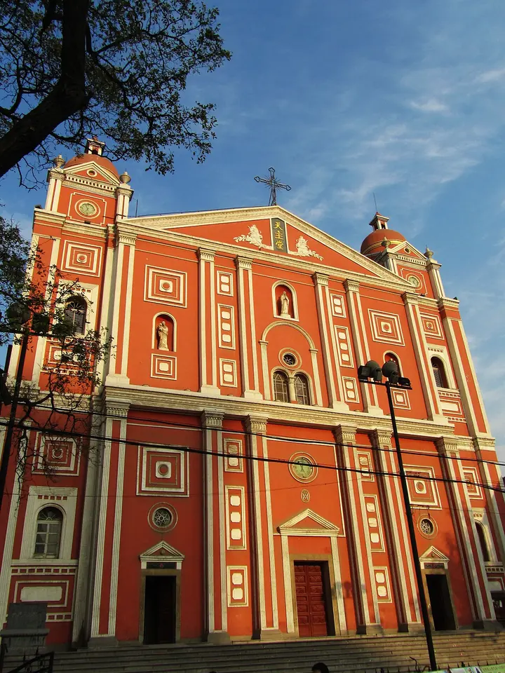 The tall red and white facade of the Catholic cathedral in Taiyuan with two towers and a cross, under a blue sky