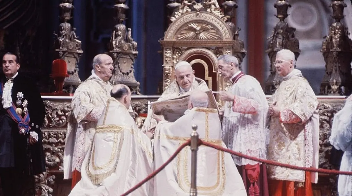 Color photograph of the elderly pope in a white and gold cope and miter at the altar of St. Peter's, surrounded by bishops in white miters