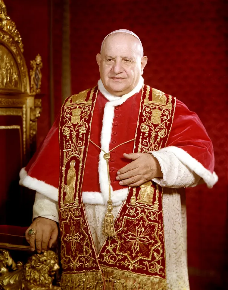 Color photograph of Pope John XXIII standing beside a gilded chair in a red velvet mozzetta trimmed with white fur and a gold-embroidered red stole