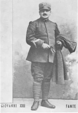 Old black-and-white studio photograph of a young mustached soldier in a World War I Italian army uniform and cap, holding a coat over one arm