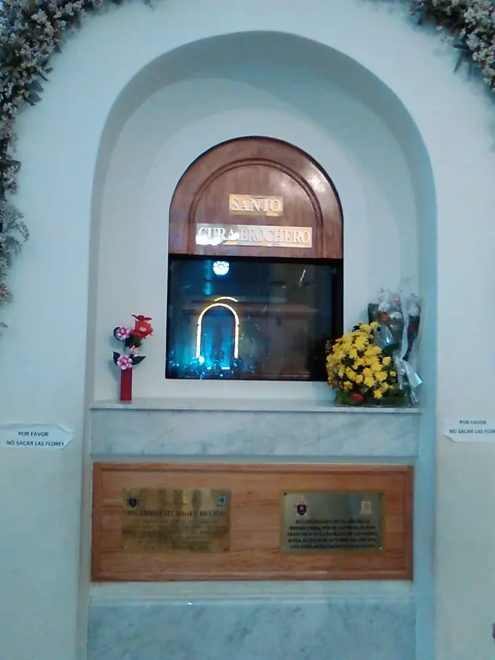 A white marble wall niche with a small arched window, flowers on either side and bronze plaques below