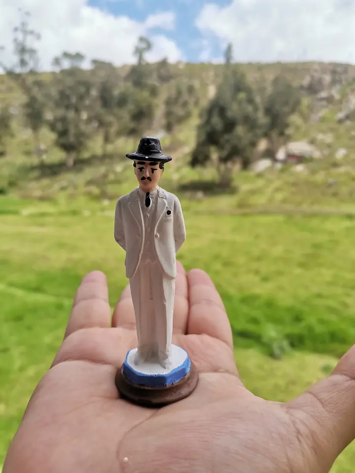 A small painted figurine of Dr. Hernández in a white suit and black hat held in the palm of a hand against a green hillside
