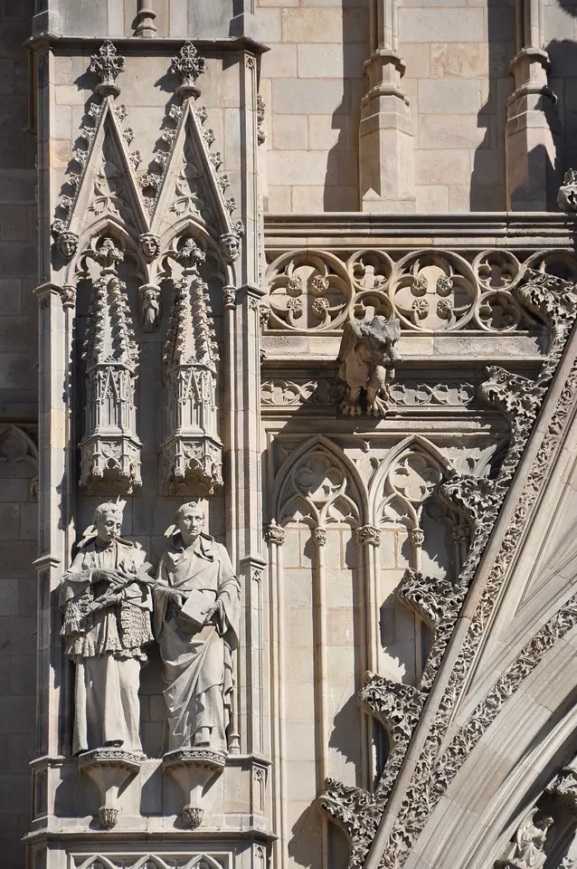 Two stone statues of saints in clerical robes standing side by side in a niche on the carved Gothic Revival facade of Barcelona Cathedral
