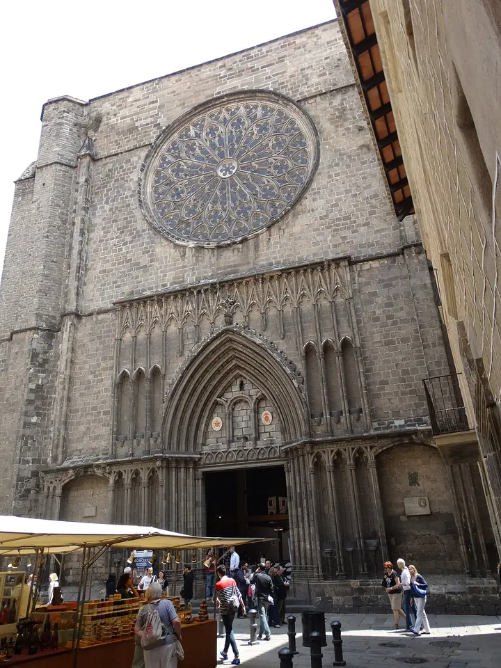 The tall, plain stone Gothic facade of Santa Maria del Pi with its great rose window above a pointed doorway, and people at market stalls in the square