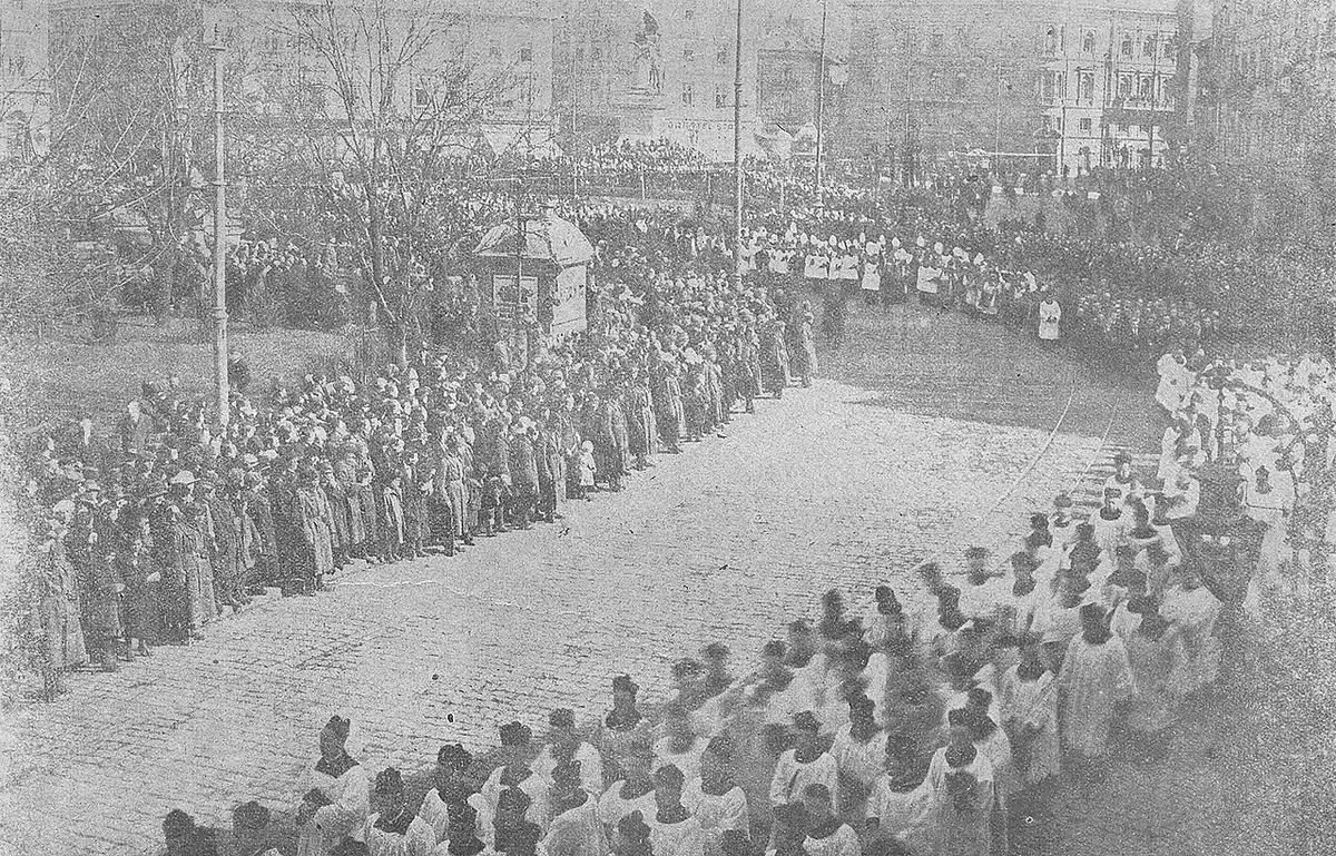 Old photograph of a huge crowd and long lines of clergy filling a city square for a funeral procession