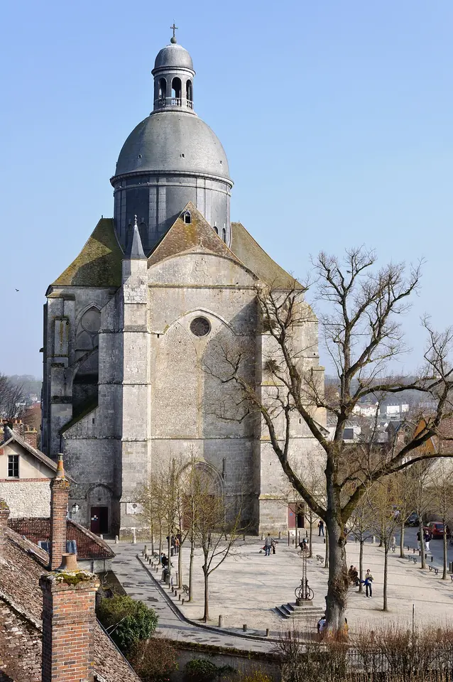 A large Gothic church with a gray dome above its crossing, rising over a square with bare trees in the medieval town of Provins