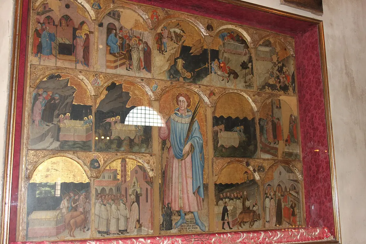 A gilded painted altarpiece divided into many small arched scenes around a standing figure of a young saint in the center, inside a red frame
