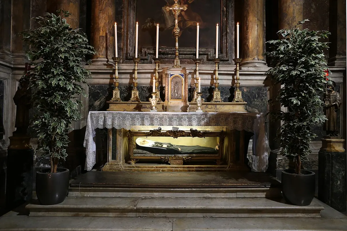 Marble altar with six tall candlesticks and a crucifix, with a glass reliquary below the altar table holding the figure of the saint in her habit