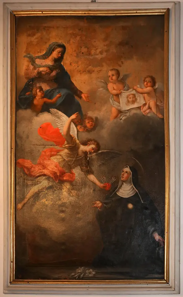 Framed painting of a kneeling nun in a black habit looking up at the Virgin and Child in the clouds, as an angel in red flies down toward her