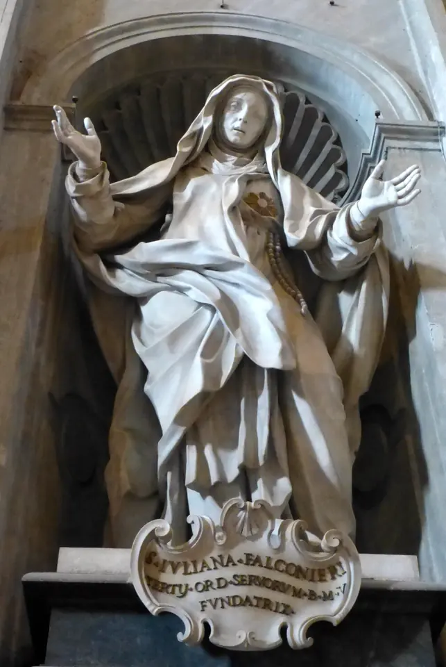 White marble statue of St. Juliana in a niche, arms opened wide, a Host on her breast, above a cartouche naming her foundress of the Servite Sisters