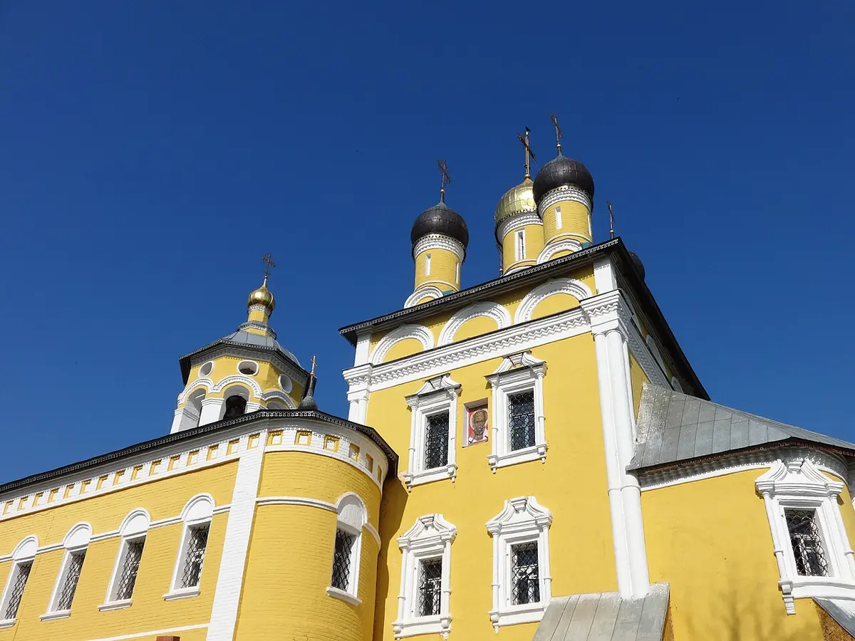 Yellow and white church with small black and gold onion domes against a deep blue sky