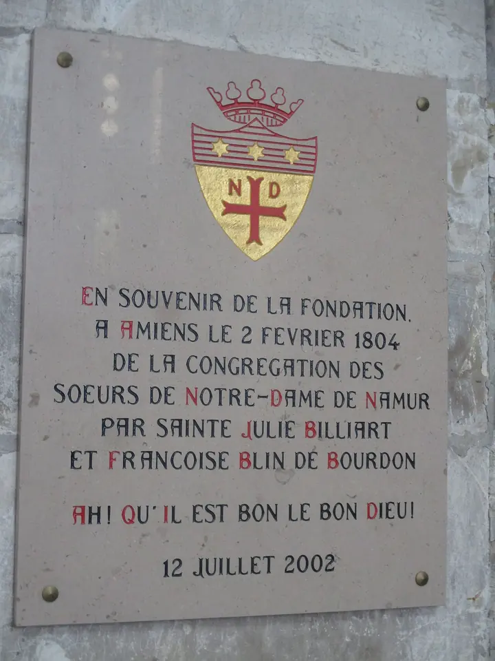 Stone plaque with a coat of arms marked ND and a cross, recording in French the founding of the Sisters of Notre-Dame de Namur at Amiens on February 2, 1804, by St. Julie Billiart and Françoise Blin de Bourdon, with the words Ah! qu'il est bon le bon Dieu!