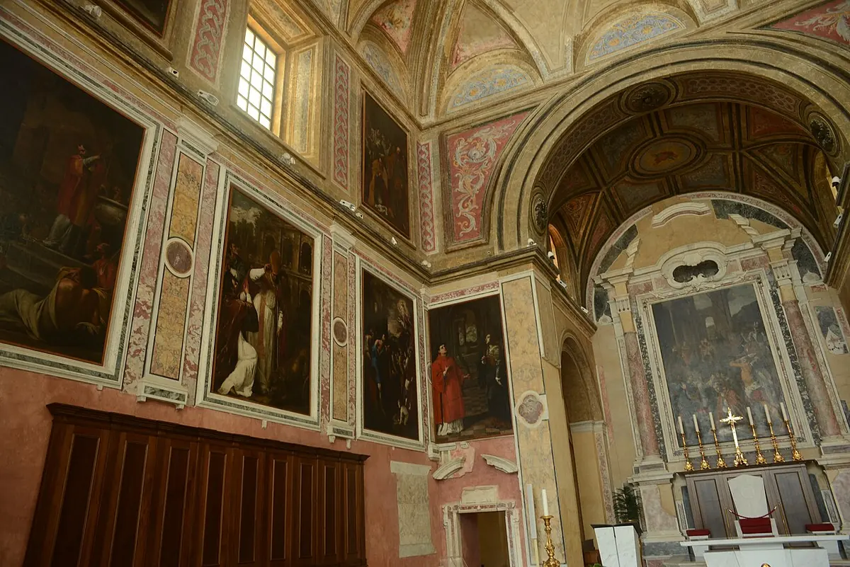 The interior of a cathedral with old paintings on pink marble walls, wooden choir stalls and a side altar with a large altarpiece