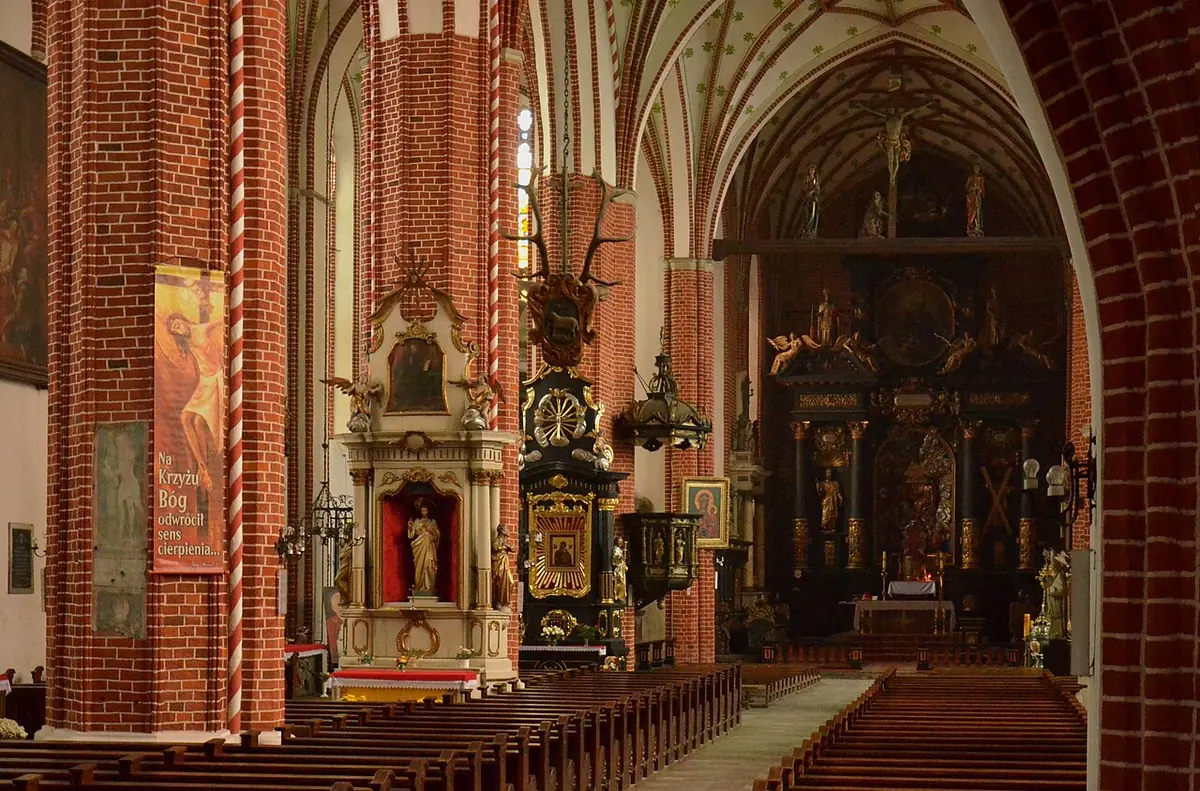 The tall red-brick Gothic nave of a cathedral with carved Baroque altars along the pillars and a gilded high altar at the far end