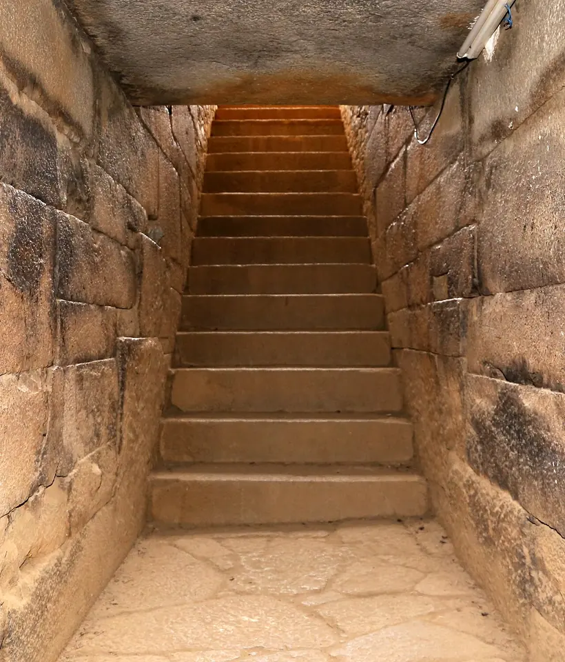 Narrow stone stairway of finely fitted granite blocks leading up out of an underground tomb toward daylight