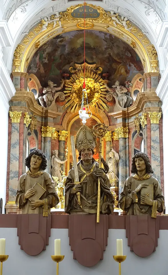 Three carved wooden figures of the Franconian apostles, a bishop between two young clerics, in front of the gilded Baroque high altar of the Neumünster