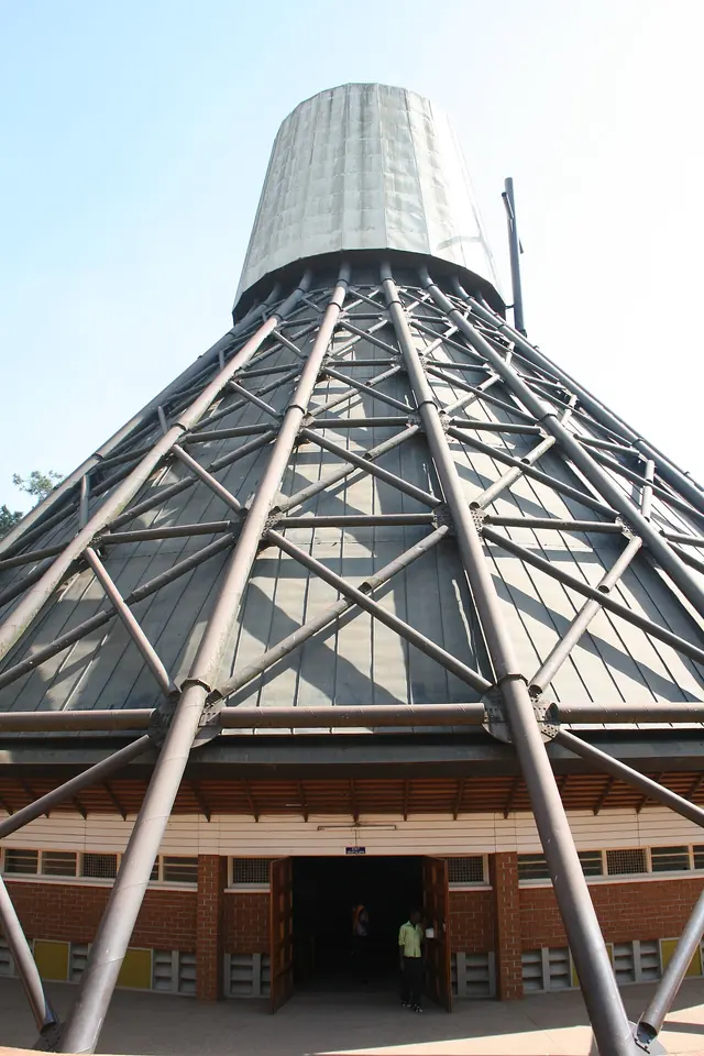 The cone-shaped roof of the Namugongo basilica rising on a lattice of slanting steel columns, seen from close to the entrance