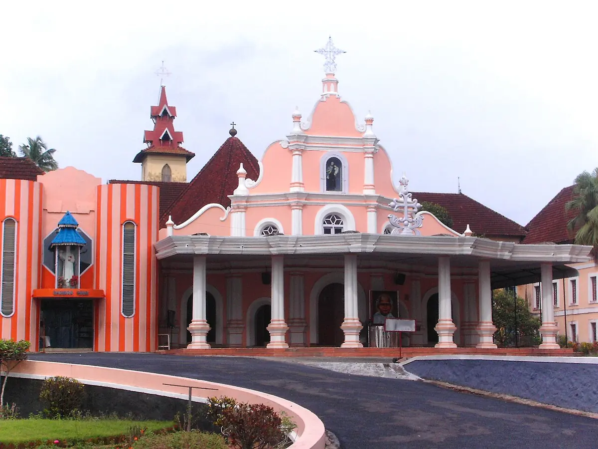 The pink and white facade of St. Joseph's Monastery Church at Mannanam with a covered porch and a curving drive